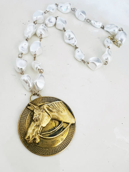 Necklace with gold horse pendant and white pearls on a light background