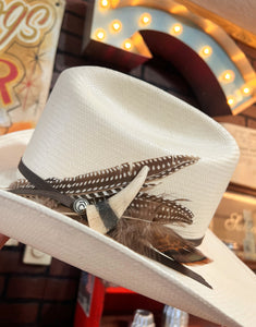 White cowboy hat with feathers and a band against a blurred background