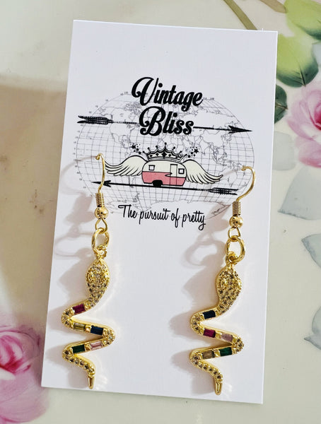 Gold snake-shaped earrings on a 'Vintage Bliss' branded card with floral background