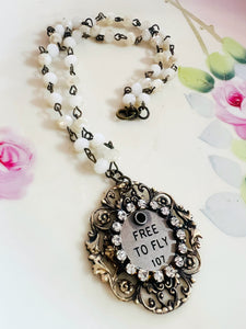 Necklace with decorative pendant and 'FREE TO FLY' text on a floral background