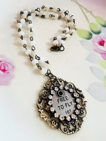 Necklace with decorative pendant and 'FREE TO FLY' text on a floral background