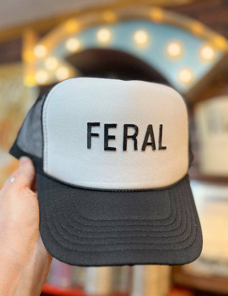 Black and white cap with 'FERAL' text held in front of a blurred indoor background