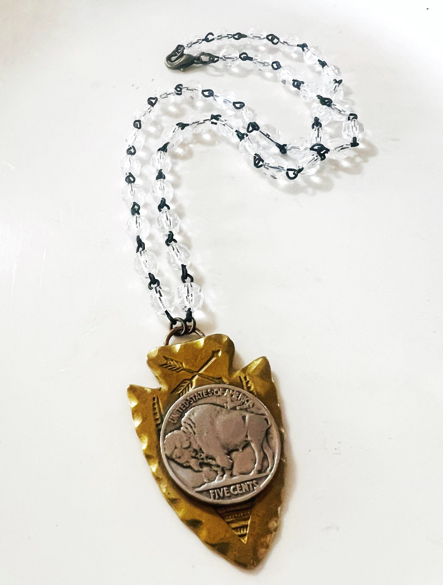 Necklace with a gold arrowhead pendant featuring a coin with a buffalo design on a white background