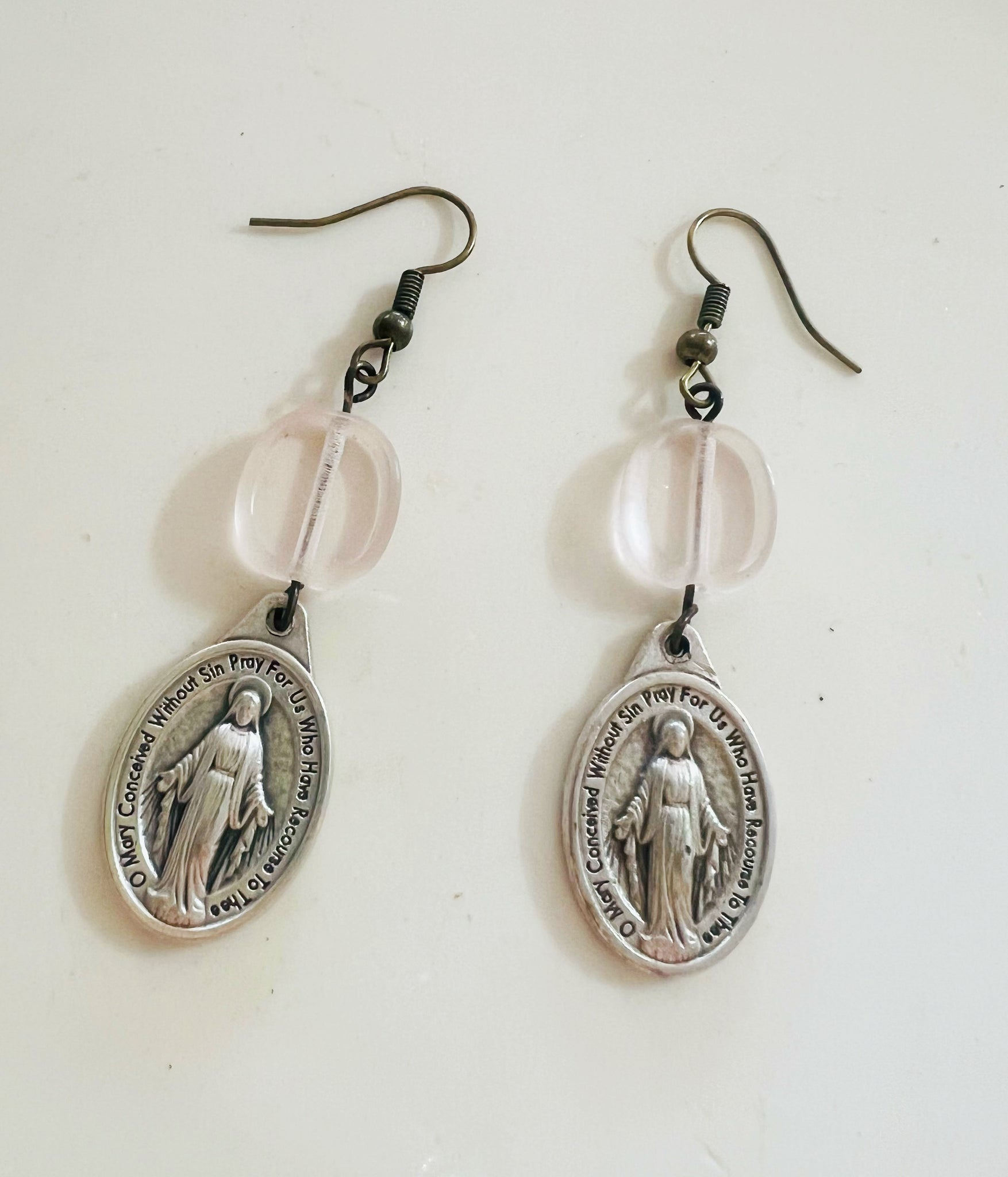 Pair of silver religious earrings with clear beads on a white background