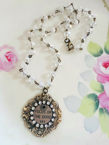 Necklace with a pendant that says 'Focus on the Good' on a floral background