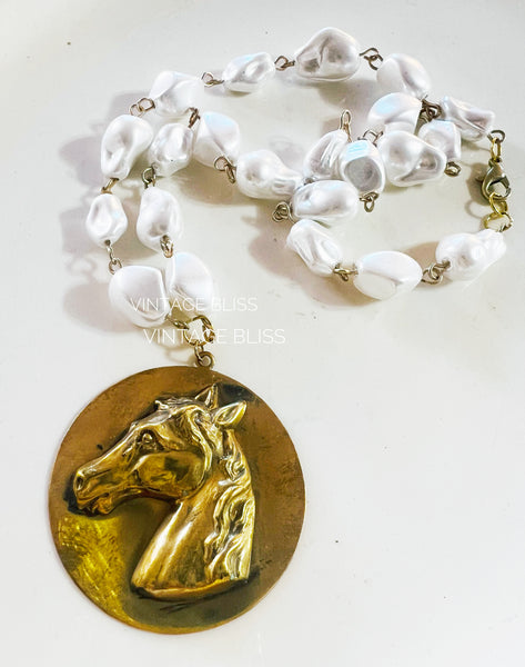 Necklace with white beads and a gold horse head pendant on a white background