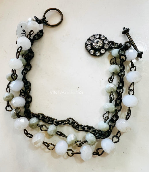 Multistrand bracelet with white beads and black chain on a light background